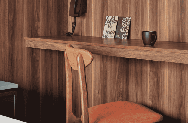  Wood-paneled desk and orange chair in the balcony room at Grandi by Center Hotels in Reykjavik, with coffee mug and printed postcards.