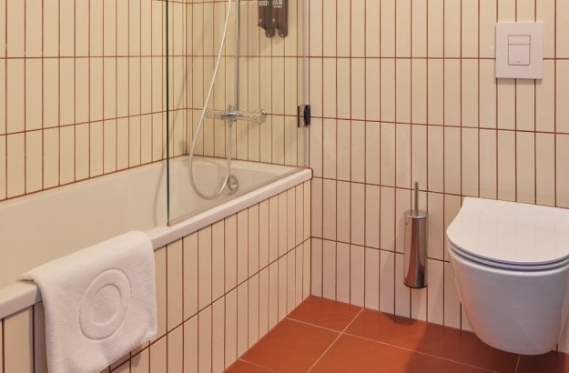 Bathroom in the standard plus room at Grandi by Center Hotels featuring a tiled bathtub with glass partition and wall-mounted toilet.