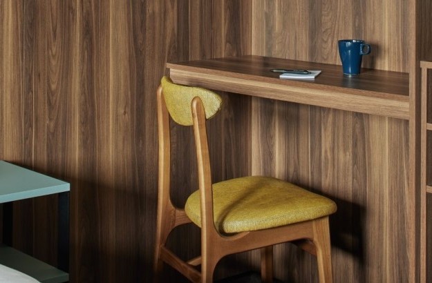 Work desk in the deluxe king room at Grandi by Center Hotels in Reykjavik with wood paneling, yellow chair, and ceramic mug.
