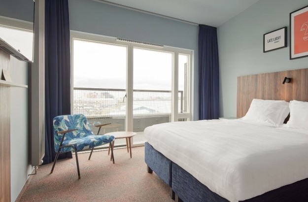 Balcony room at Grandi by Center Hotels in Reykjavik with kind bed, wall art, and large window doors opening to private balcony.