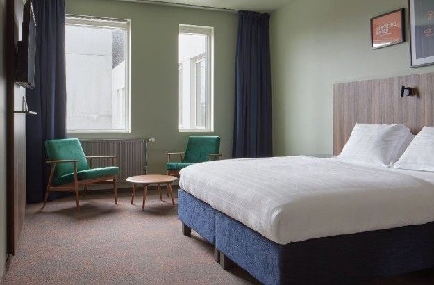 Full view of the deluxe king room at Grandi by Center Hotels in Reykjavik featuring a king-size bed, green armchairs, and wall art.