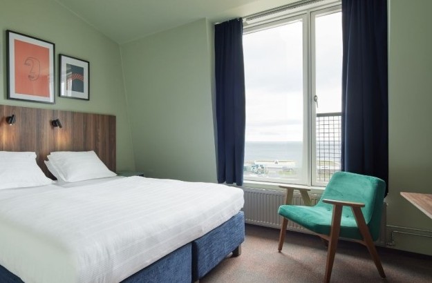 Standard double/twin room at Grandi by Center Hotels featuring a soft green color, large window, and modern artwork above the bed.