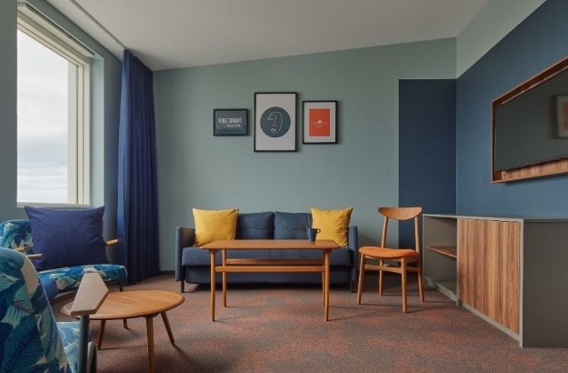  Living room area in the suite at Grandi by Center Hotels in Reykjavik featuring navy sofa, yellow pillows, wall art, and a wall-mounted TV.