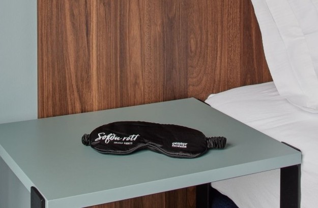 Close-up of bedside table in balcony room at Grandi by Center Hotels in Reykjavik with branded sleep mask and wood headboard.