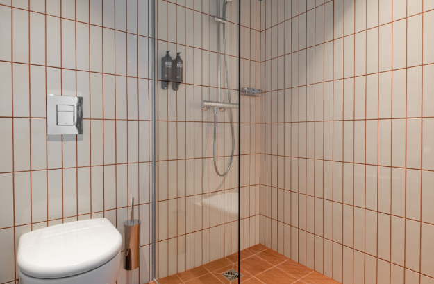A picture of the bathroom in a standard room at Grandi by Center Hotels in Reykjavík with a walk-in shower, shampoo, conditioner and a toilet. 