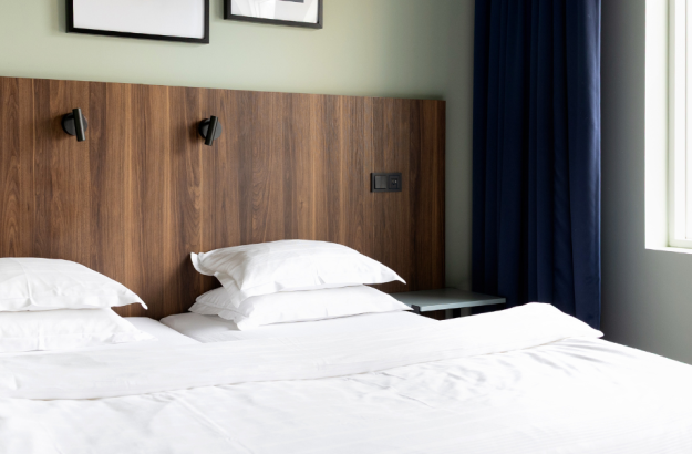 Bed in standard plus room at Grandi by Center Hotels with white sheets and wooden headboard.
