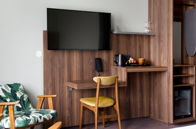 Desk area in standard plus room at Grandi by Center Hotels in Reykjavik with wooden table, yellow chair, flat screen TV, ironing board and a mini fridge.