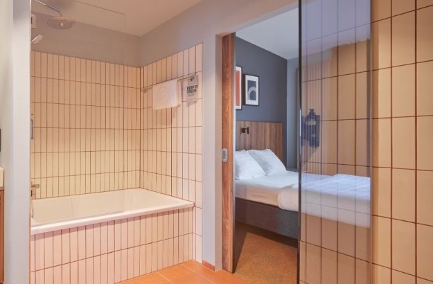 Bathtub and wood vanity in the suite bathroom at Grandi by Center Hotels in Reykjavik, with warm tiling and glass divider.