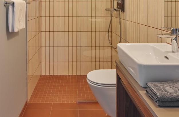 Modern bathroom in the suite at Grandi by Center Hotels in Reykjavik with wall-mounted sink, white vertical tiles and glass shower enclosure.