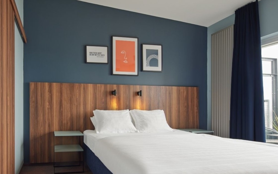 Suite bedroom at Grandi by Center Hotels in Reykjavik with navy blue wall, framed artwork, and wooden headboard.
