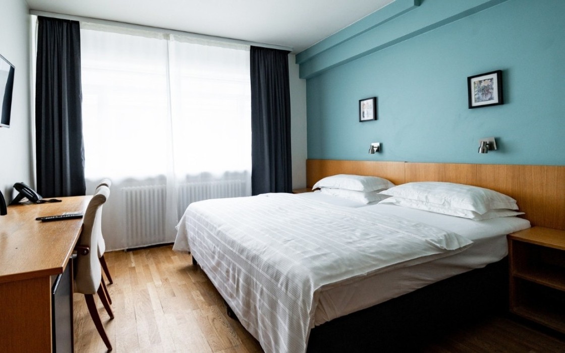 Standard double room at Center Hotels Klopp in Reykjavik, with a large bed, teal-colored accent wall, window with blackout curtains, desk, and mounted TV.