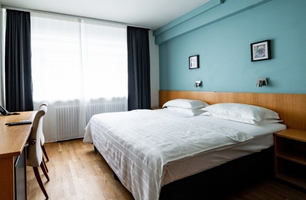 Standard double room at Center Hotels Klopp in Reykjavik, with a large bed, teal-colored accent wall, window with blackout curtains, desk, and mounted TV.