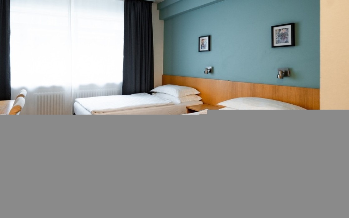 Standard twin room at Center Hotels Klopp in Reykjavik, with two single beds, teal accent wall, wooden headboard, and a window with blackout curtains.