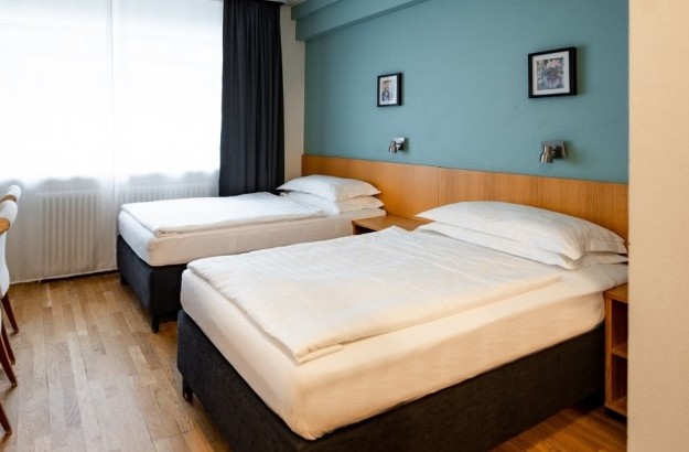 Standard twin room at Center Hotels Klopp in Reykjavik, with two single beds, teal accent wall, wooden headboard, and a window with blackout curtains.