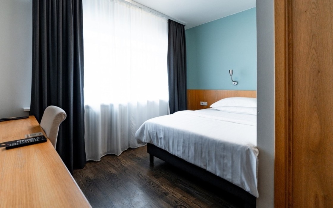 Standard single room at Center Hotels Klopp in Reykjavik, with a neatly made bed, large window with curtains, and wooden desk with chair and TV.