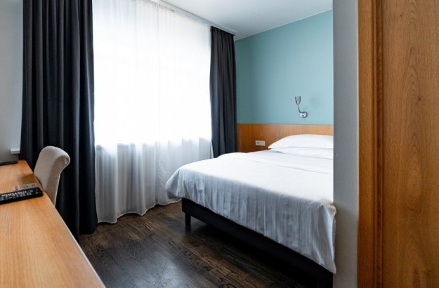 Standard single room at Center Hotels Klopp in Reykjavik, with a neatly made bed, large window with curtains, and wooden desk with chair and TV.