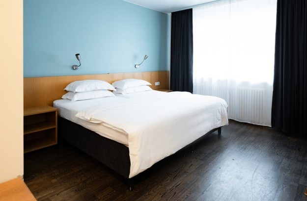 Superior double room at Center Hotels Klopp featuring a king-sized bed, large window with blackout curtains, and a desk for two.