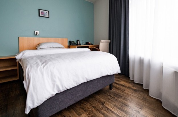 Bright superior single room at Center Hotels Klopp in Reykjavik, featuring a single bed with white bedding, wood flooring, minimalist furniture, and large windows letting in natural light.