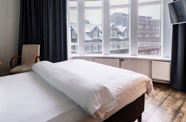 Superior single room at Center Hotels Klopp in Reykjavik with a large window wall overlooking city buildings, a bed with white linen, a work desk, and natural lighting.