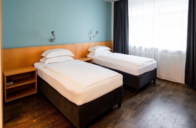 Superior twin room at Center Hotels Klopp in Reykjavik with two single beds against a teal accent wall, nightstands, and dark wood flooring.