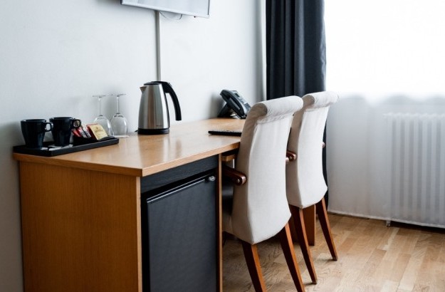Desk area in a standard room at Center Hotels Klopp, featuring a kettle, mugs, wine glasses, minibar, telephone, and flat-screen TV mounted on the wall.