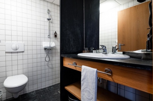 Bathroom in a standard single room at Center Hotels Klopp in Reykjavik, featuring a tiled walk-in shower, wall-mounted toilet, and black countertop with sink and amenities.