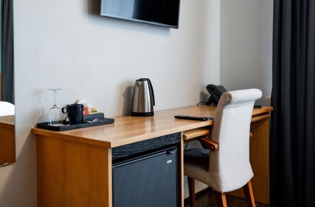 In-room amenities in a standard single room at Center Hotels Klopp, including a kettle, mugs, glassware, and minibar on a wooden desk with a wall-mounted TV above.