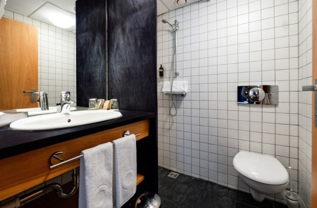 Bathroom in a standard room at Center Hotels Klopp in Reykjavik, featuring a walk-in shower, wall-mounted toilet, dark countertop sink, and hotel toiletries.