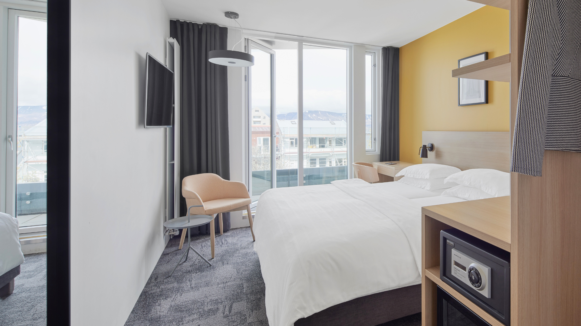 Balcony room with yellow wall, double bed, large window, balcony and mountain view at Center Hotels Laugavegur in Reykjavik.