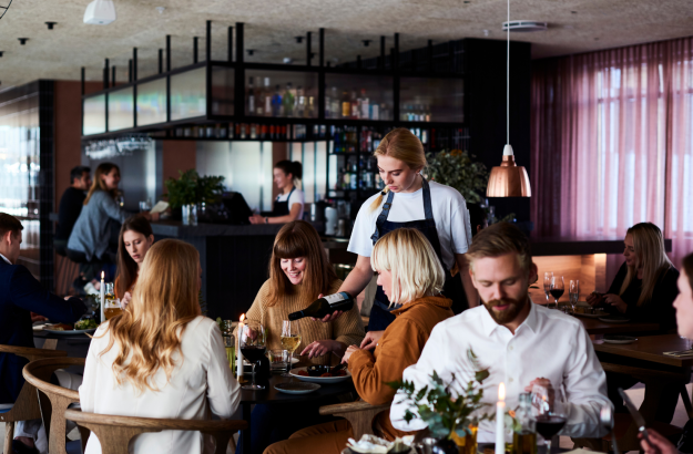 Group of guests dining at Lóa Restaurant at Center Hotels Laugavegur in Reykjavik with wine being poured at a table and bartender in background.