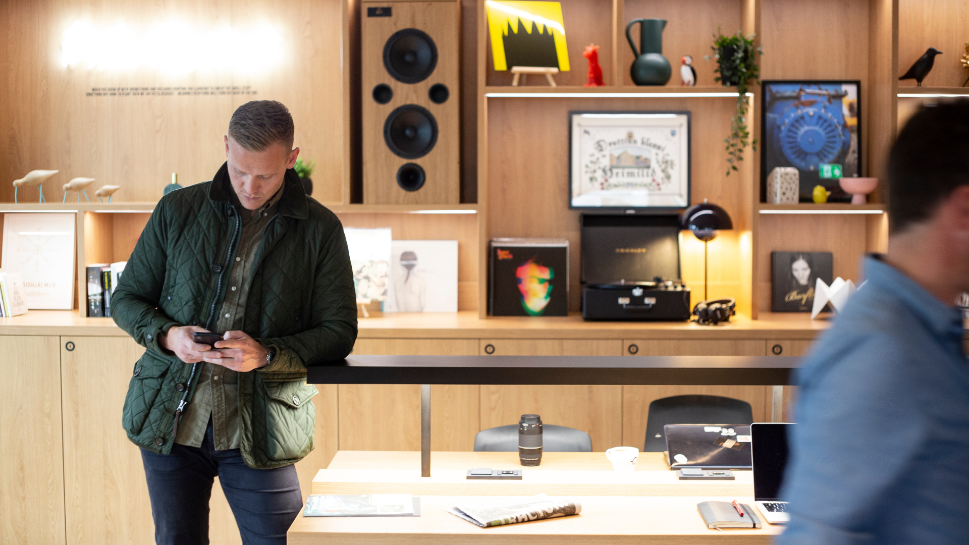 Guest using phone at stylish communal workspace with vinyl records and Scandinavian design at Center Hotels Laugavegur in Reykjavik.