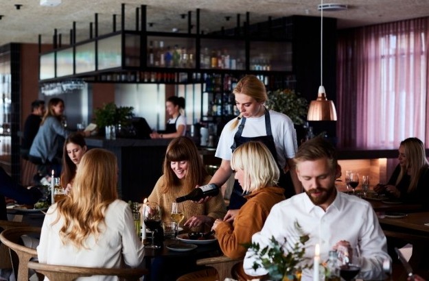 Group of guests dining at Lóa Restaurant at Center Hotels Laugavegur in Reykjavik with wine being poured at a table and bartender in background.