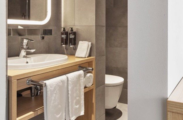 Bathroom with sink, illuminated mirror, mounted soap dispensers and grey tiled walls at Center Hotels Laugavegur in Reykjavik.