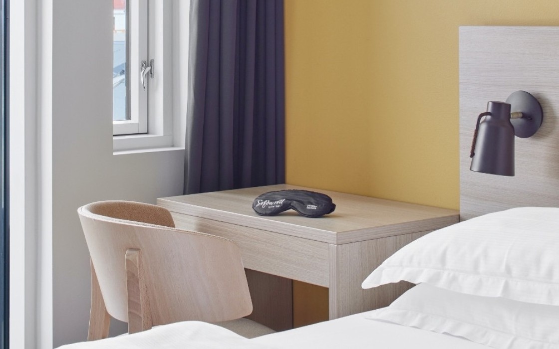 centerhotels-laugavegur-reykjavik-balcony-room-desk Alt: Wooden desk and chair next to bed and glass door leading to private balcony at Center Hotels Laugavegur in Reykjavik.