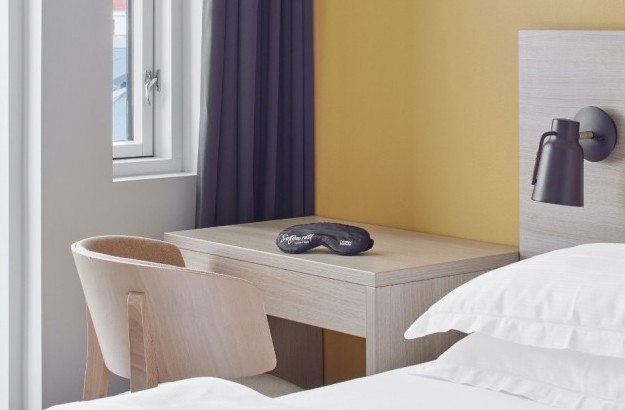 centerhotels-laugavegur-reykjavik-balcony-room-desk Alt: Wooden desk and chair next to bed and glass door leading to private balcony at Center Hotels Laugavegur in Reykjavik.