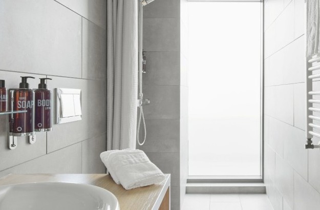 Bathroom in deluxe corner room at Center Hotels Laugavegur in Reykjavik with grey tiles, backlit mirror, mounted toiletries and heated towel rack.