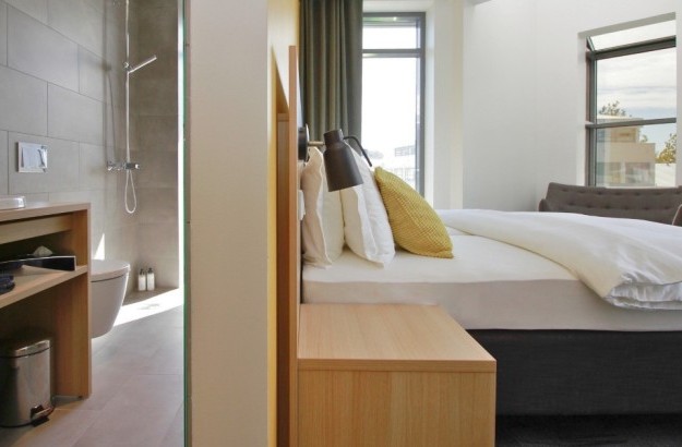 Deluxe corner room at Center Hotels Laugavegur in Reykjavik a bathroom sink, walk-in shower, bed with yellow cushions and a large window.