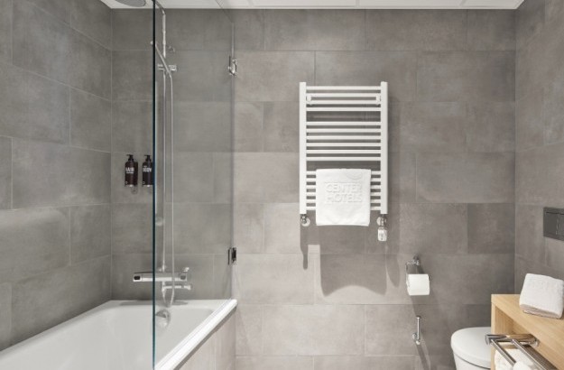 Bathroom in deluxe room at Center Hotels Laugavegur in Reykjavik with bathtub, glass shower divider, heated towel rack and grey tiled walls.