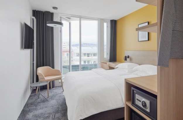 centerhotels-laugavegur-reykjavik-balcony-room-overview Alt: Balcony room with yellow wall, double bed, large window, balcony and mountain view at Center Hotels Laugavegur in Reykjavik.