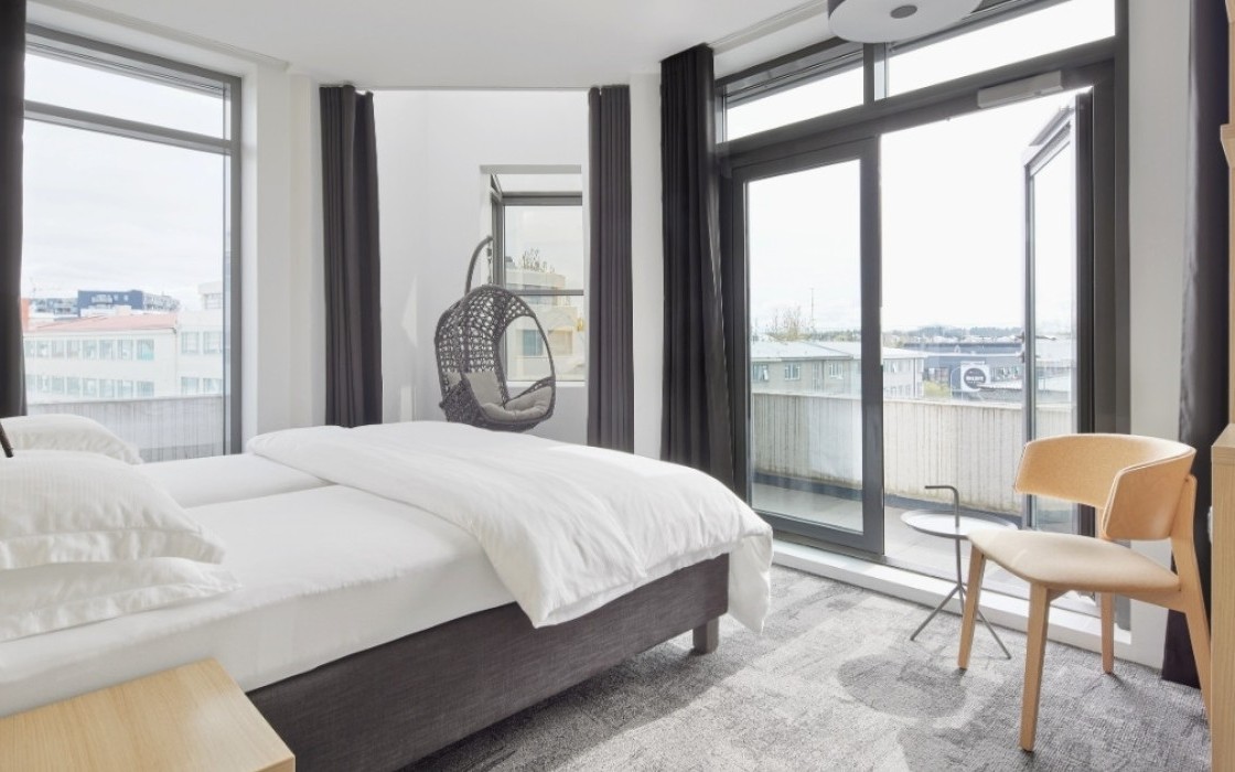 Deluxe corner room at Center Hotels Laugavegur in Reykjavik with bed, balcony access, coffee station, and grey hanging chair by the window.