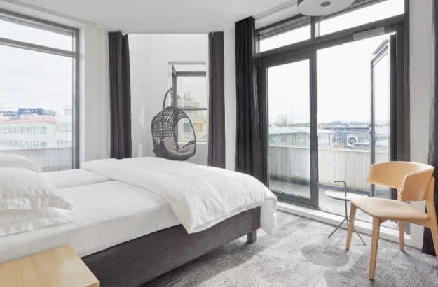 Deluxe corner room at Center Hotels Laugavegur in Reykjavik with bed, balcony access, coffee station, and grey hanging chair by the window.
