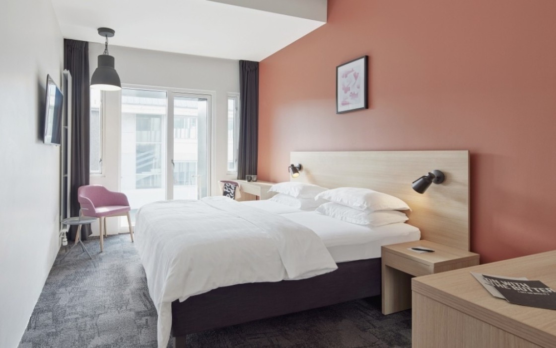 Deluxe room at Center Hotels Laugavegur in Reykjavik with double bed, pink accent wall, TV, balcony, and a pink lounge chairs.