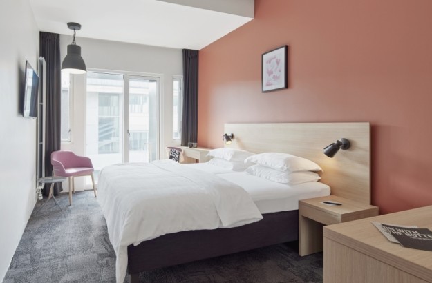 Deluxe room at Center Hotels Laugavegur in Reykjavik with double bed, pink accent wall, TV, balcony, and a pink lounge chairs.