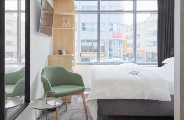 Bright small double room at Center Hotels Laugavegur in Reykjavik featuring a large window, double bed, green lounge chair, and a TV.
