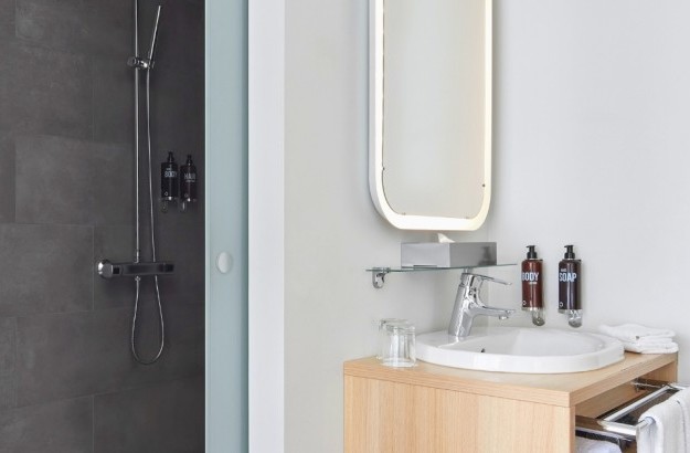 Modern bathroom with large grey-tiled walk-in shower, illuminated mirror, and mounted body care dispensers.