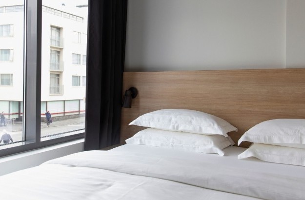 Double bed with white bedding and wooden headboard next to large window overlooking the streets of Reykjavik at Center Hotels Laugavegur.