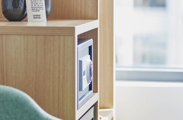 Wooden shelving unit with safe, glassware, and Center Hotels welcome card.