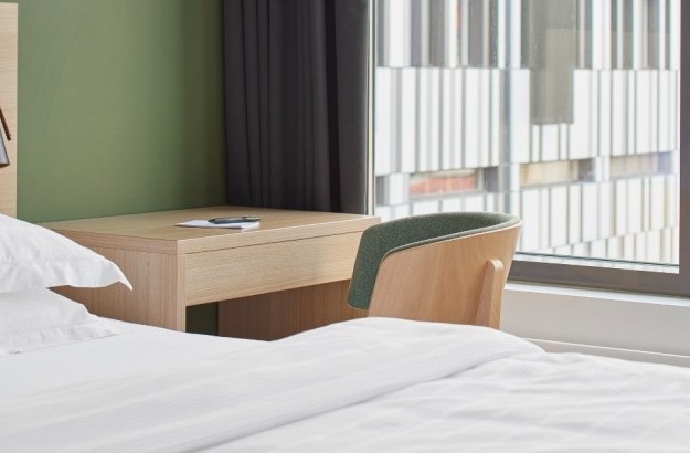 Corner of standard room at Center hotels Laugavegur in Reykjavik, with white bed linen, a wooden desk and green chair beside a large window.