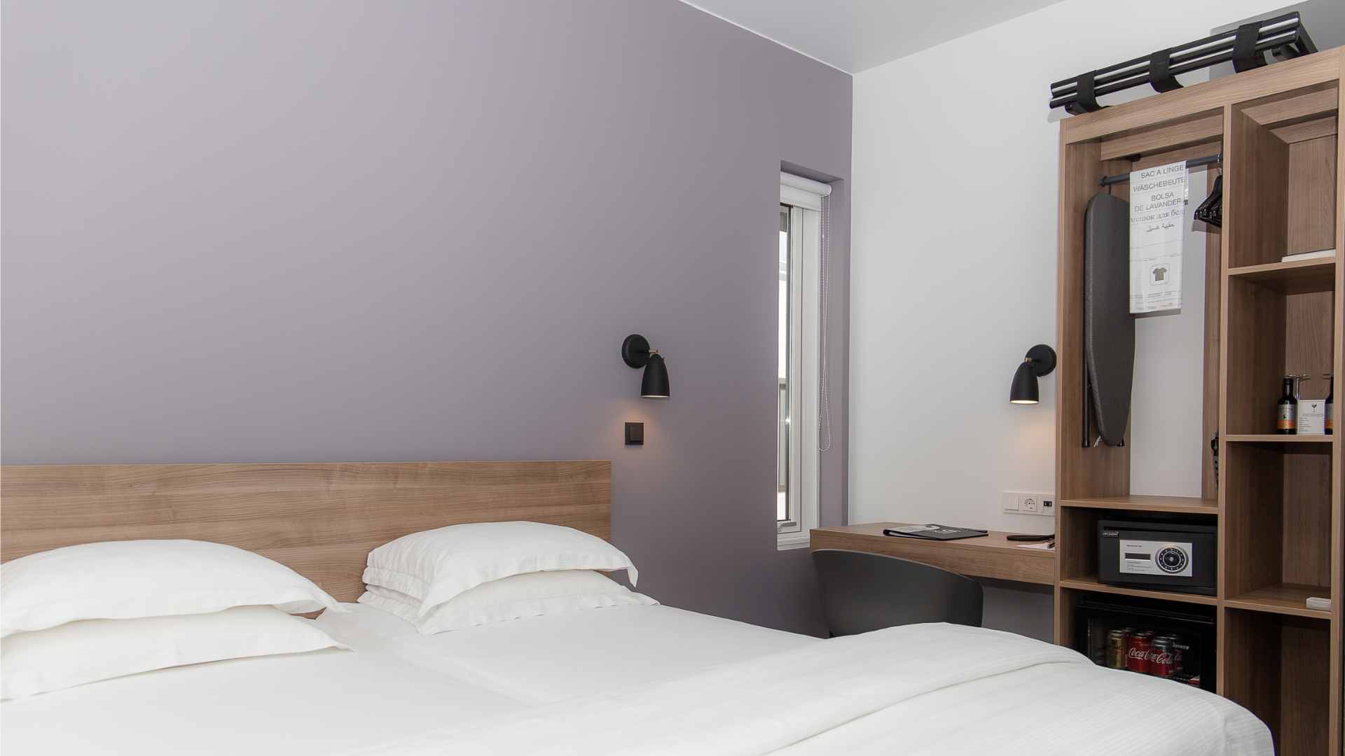 Twin bed setup with light wood headboard, integrated open closet, and compact desk in the standard room at Midgardur by Center Hotels in Reykjavik.
