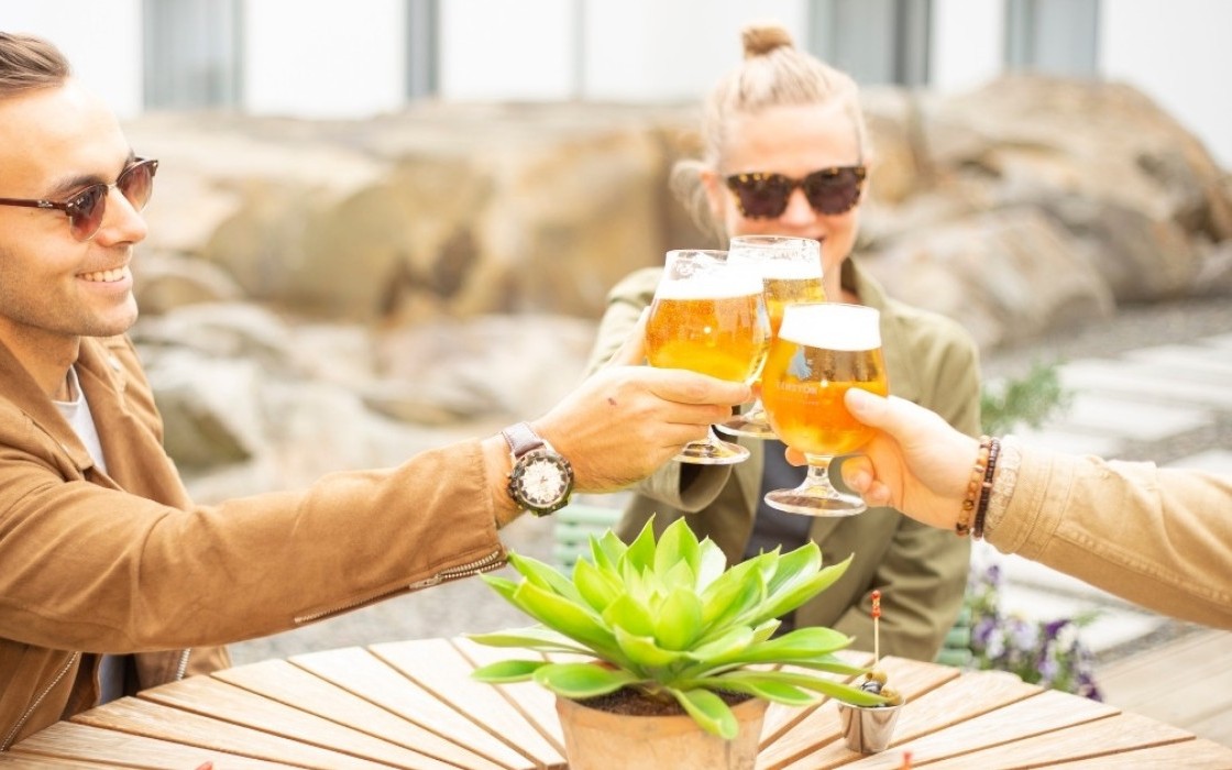 Friends enjoying a beer toast in the sunlit garden at Midgardur by Center Hotels in Reykjavik.